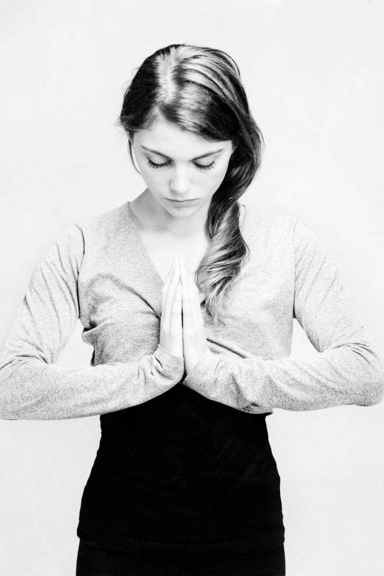 Frau in meditativer Pose mit Händen in Gebetshaltung vor der Brust.