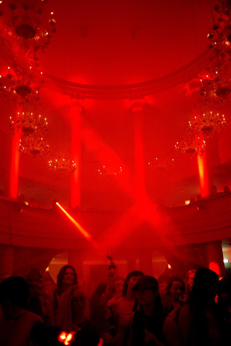 Roter Lichtstrahl in einem festlichen, gut besuchten Raum mit Kronleuchtern.