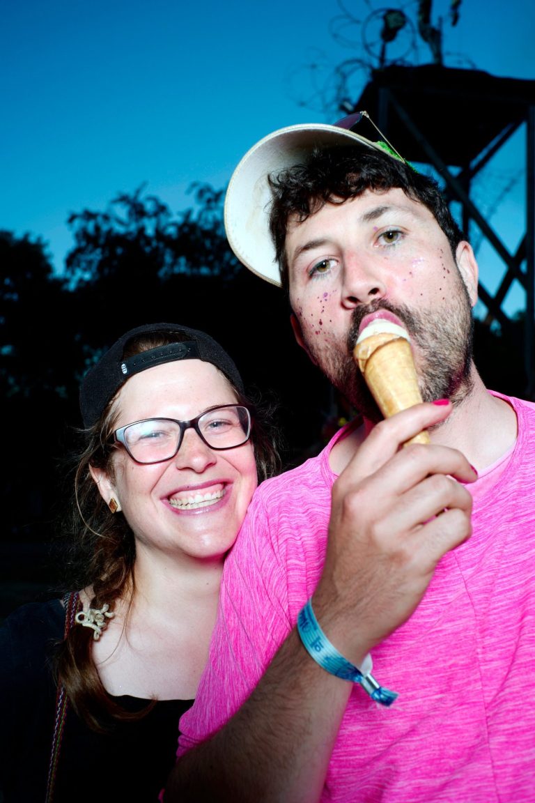Junge isst ein Eis, steht vor einer lächelnden Freundin im Freien.