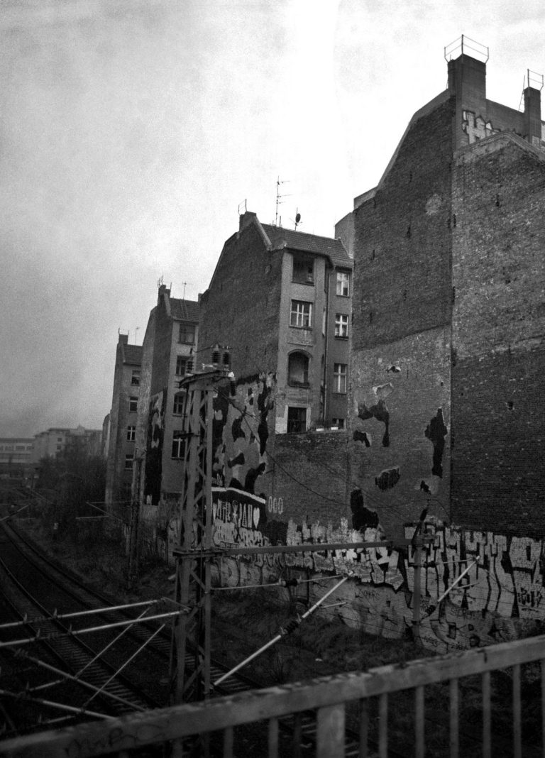 Verlassene Gebäude mit Graffiti und zerstörten Fassaden neben einer Bahnstrecke in Berlin.
