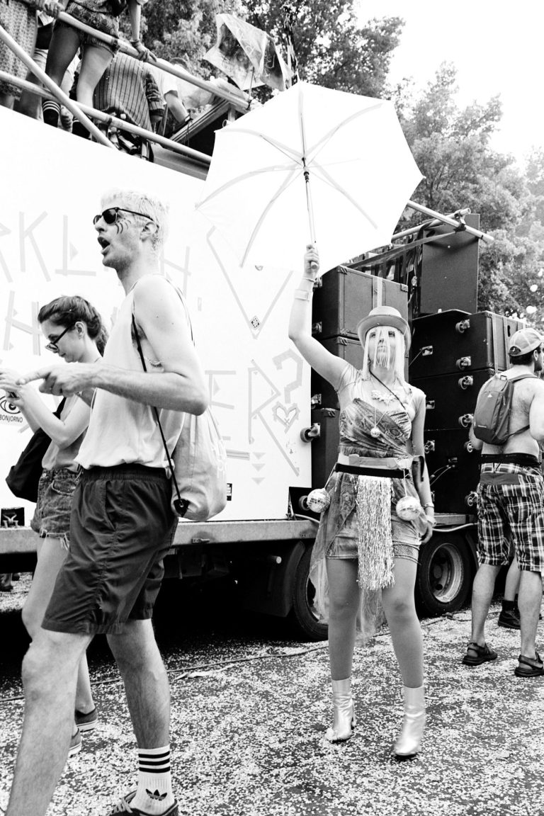Menschen bei einem Festival, ein Mädchen hält einen Sonnenschirm, andere tanzen.