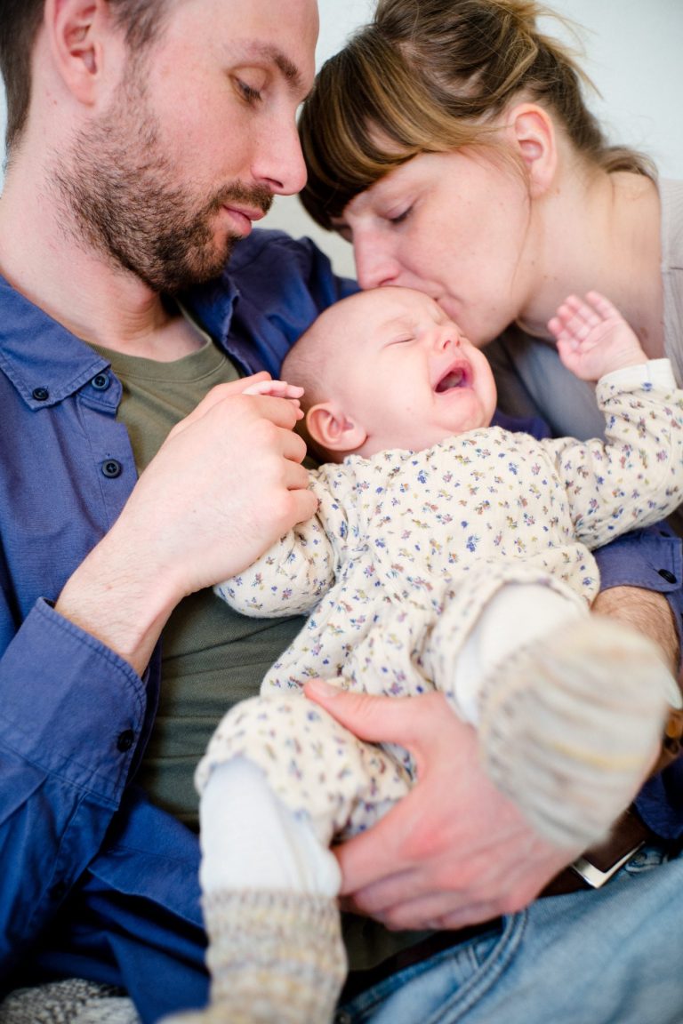 Ein Elternpaar hält ein weinendes Baby in einem gemütlichen Raum.
